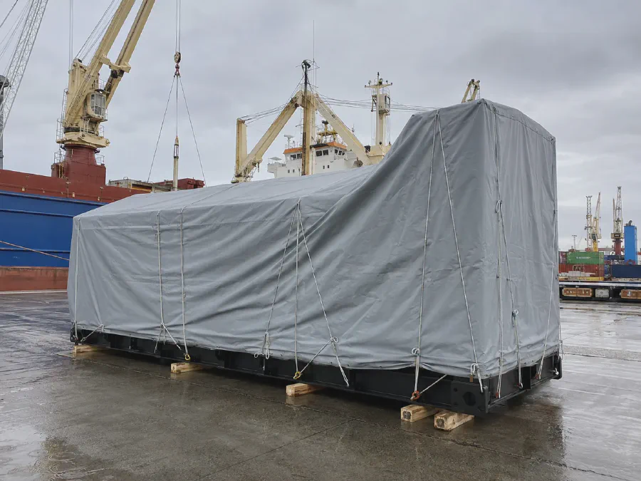 Gray tarpaulin cover protecting a generator set during port loading