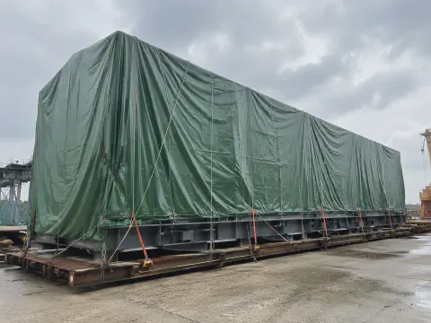 Green tarpaulin cover protecting a large steel structure module